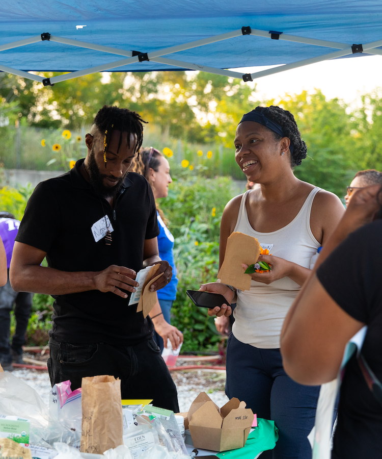 Community members talking under a tent at a seed swap and gathering at Cedillo's Fresh Produce.