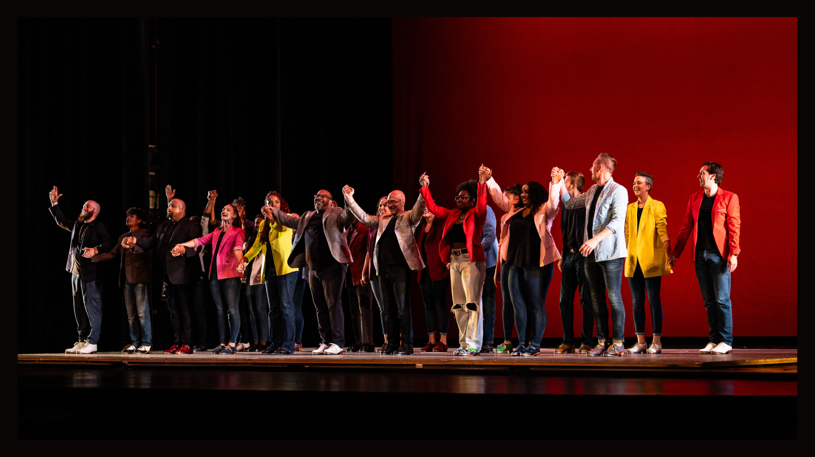 A group of people standing in a line holding hands, take a bow at the front of a stage